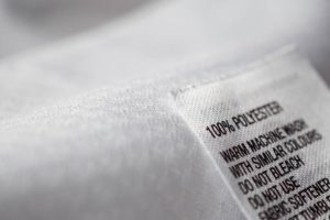 Clothing tag on white fabric stating 100% polyester with washing instructions.