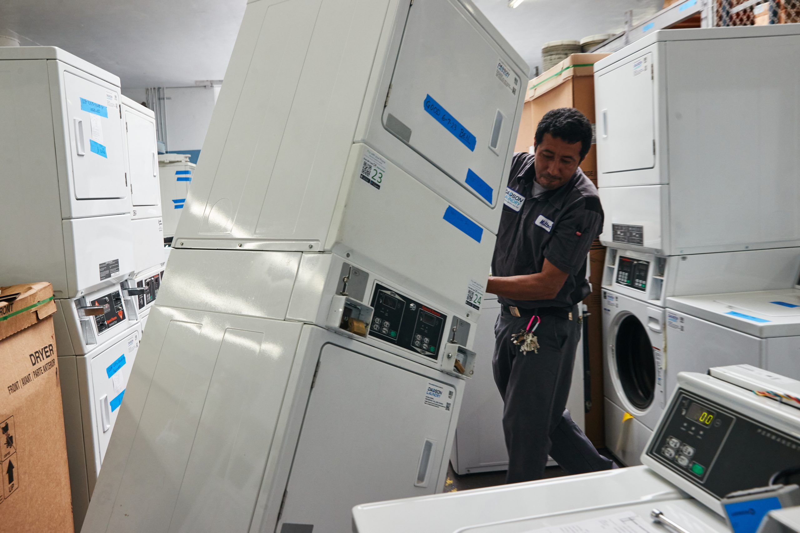 Man moving stacked laundry machines in a room filled with washing machines and dryers.