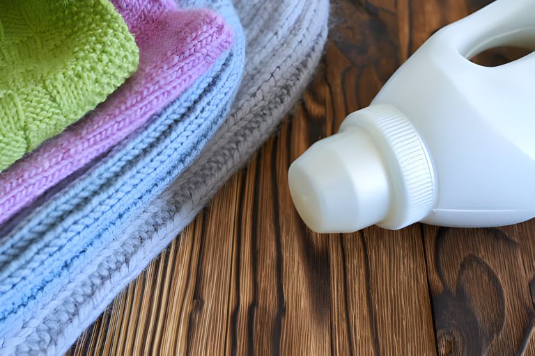 Stack of folded colorful towels next to a white plastic detergent bottle on wood.