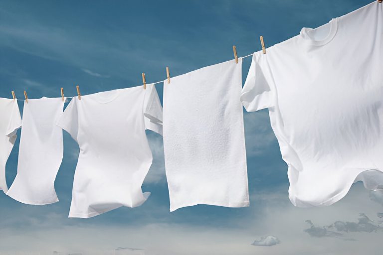 Several white t-shirts and a white cloth hanging on a clothesline against a blue sky.